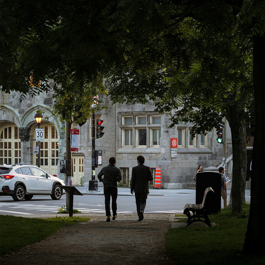 Deux piétons marchent sur un trottoir ombragé