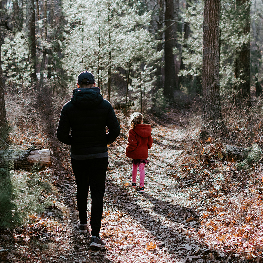 Une petite fille et son parent marchent dans un sentier de boisé urbain